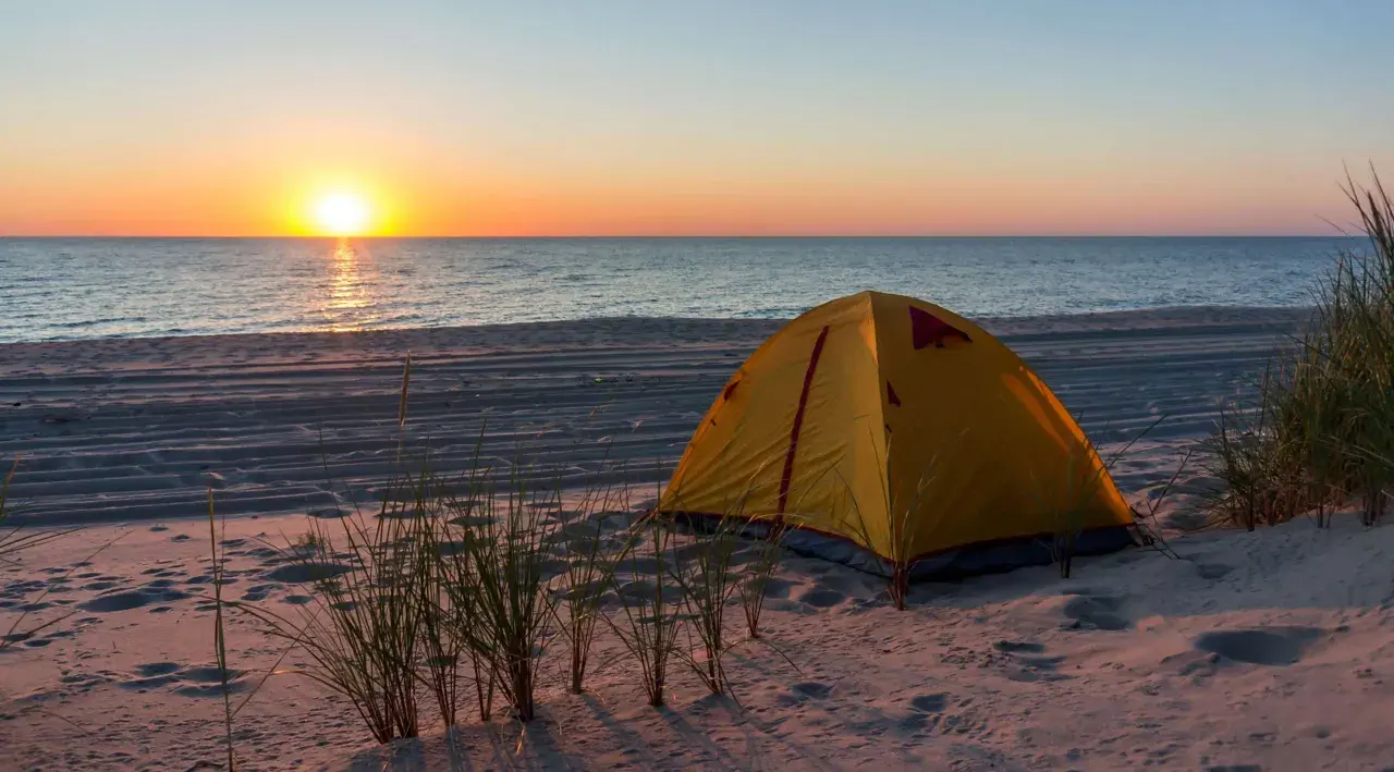 Żółty namiot na piaszczystej plaży, idealne miejsce na namioty z widokiem na zachód słońca nad morzem.