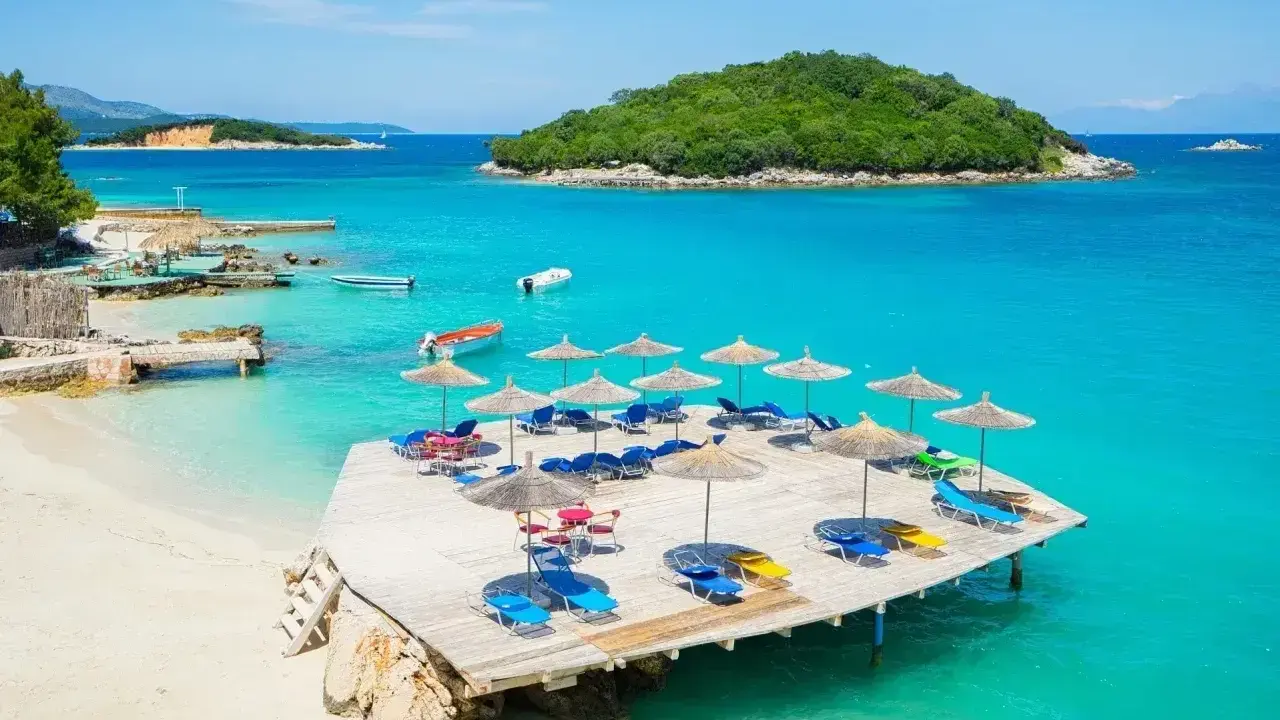 Idealne miejsce, gdzie na wakacje nad morze: piaszczysta plaża, turkusowa woda, leżaki i parasole na drewnianym pomoście.
