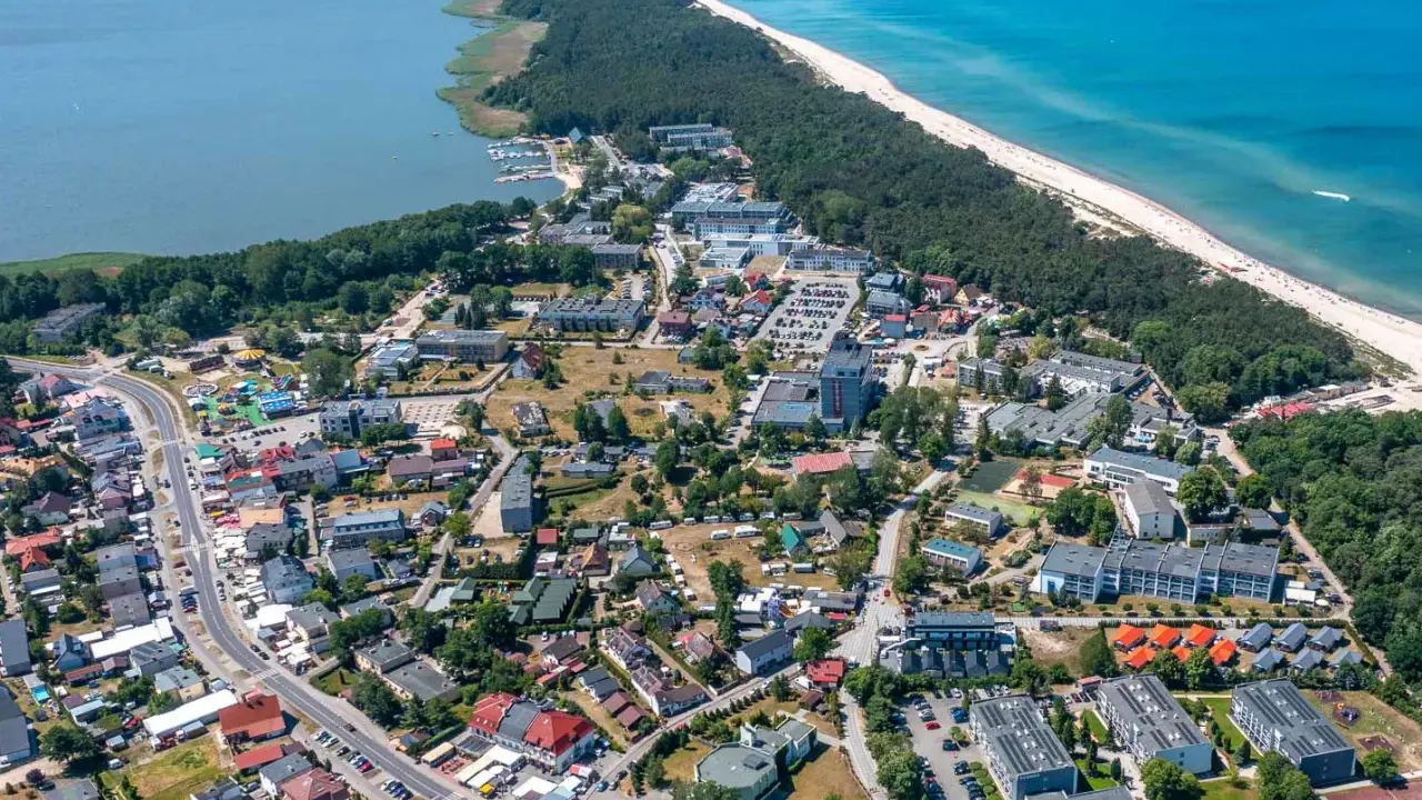 Dąbki atrakcje: widok z lotu ptaka na nadmorską miejscowość z plażą, lasem, jeziorem i zabudowaniami.