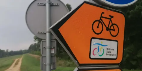 Pomarańczowy znak kierunkowy z rowerem i napisem "Wiślana Trasa Rowerowa" zapowiada podróż ścieżką wzdłuż rzeki.