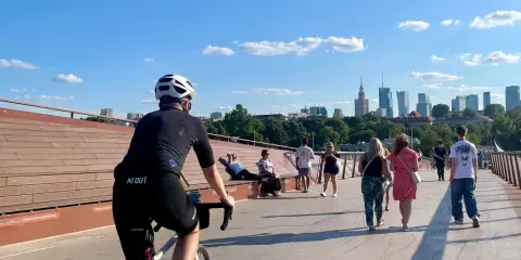 Rowerzysta na moście w Warszawie, w tle panorama miasta. Idealne miejsce na odkrywanie tras rowerowych Warszawa i okolice.