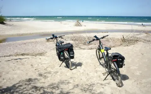 Dwa rowery z sakwami na piaszczystej plaży, gotowe na odkrywanie płaskich tras rowerowych nad morzem.