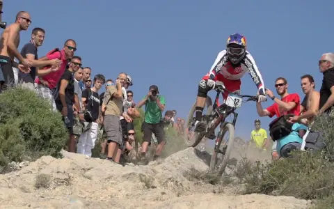 Kolarz w akcji podczas zawodów MTB, otoczony przez kibiców i fotografów.