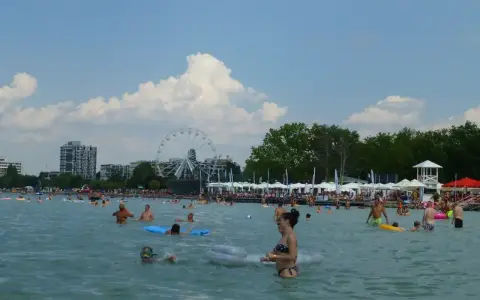 Tłum ludzi cieszy się słońcem i wodą na **Balaton plaża**. W tle widać diabelski młyn i budynki.