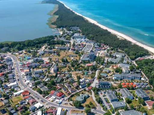 Dąbki atrakcje: widok z lotu ptaka na nadmorską miejscowość z plażą, lasem, jeziorem i zabudowaniami.