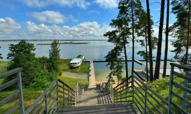Drewniane schody prowadzą do jeziora, gdzie cumuje statek. Idealne miejsce, by zapytać: gdzie na Mazury?