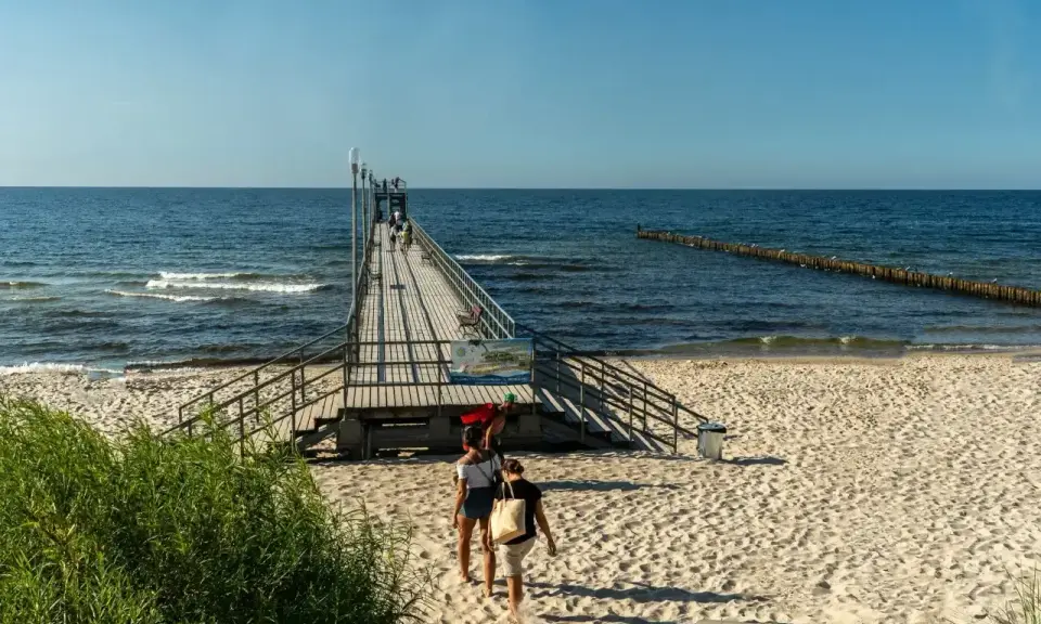 Sianożęty atrakcje: drewniane molo wchodzi w morze, plaża i fale.