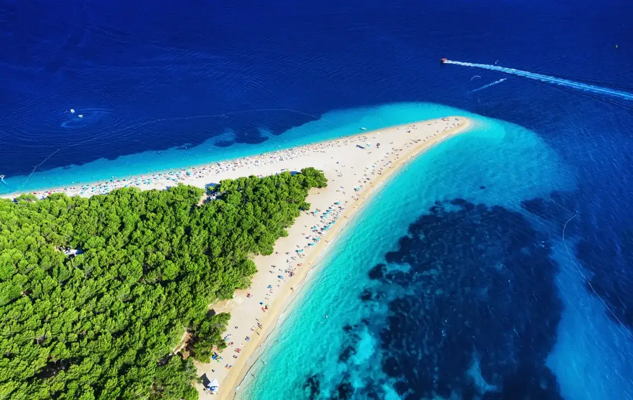 Plaża Zlatni Rat na Braču, Chorwacja, to jedno z najlepszych miejsc na wakacje. Woda jest krystalicznie czysta, a plaża otoczona sosnowym lasem.