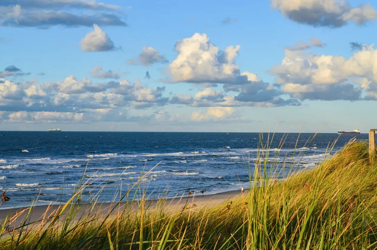 Piękne morze w Niemczech. Falujące fale, piaszczysta plaża i statki na horyzoncie pod błękitnym niebem z chmurami.