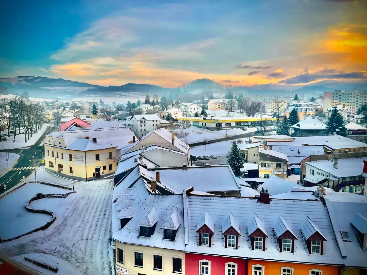 Zimowy krajobraz miasta w Czechach blisko granicy. Pokryte śniegiem dachy, g&oacute;rzyste tło i zachodzące słońce tworzą malowniczy widok.