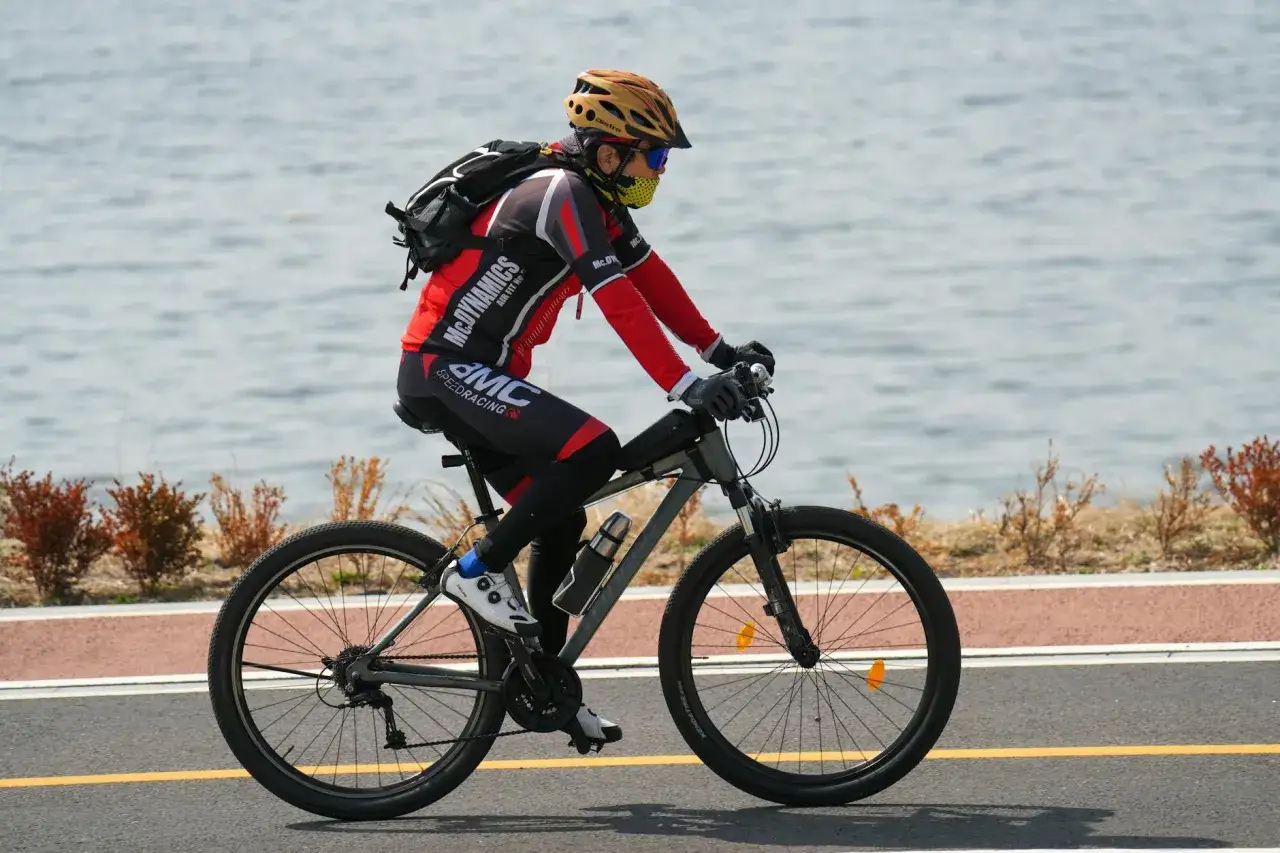 Rowerzysta w kasku i masce jedzie ścieżką nad wodą. Idealne noclegi dla rowerzyst&oacute;w czekają po wyczerpującej trasie.