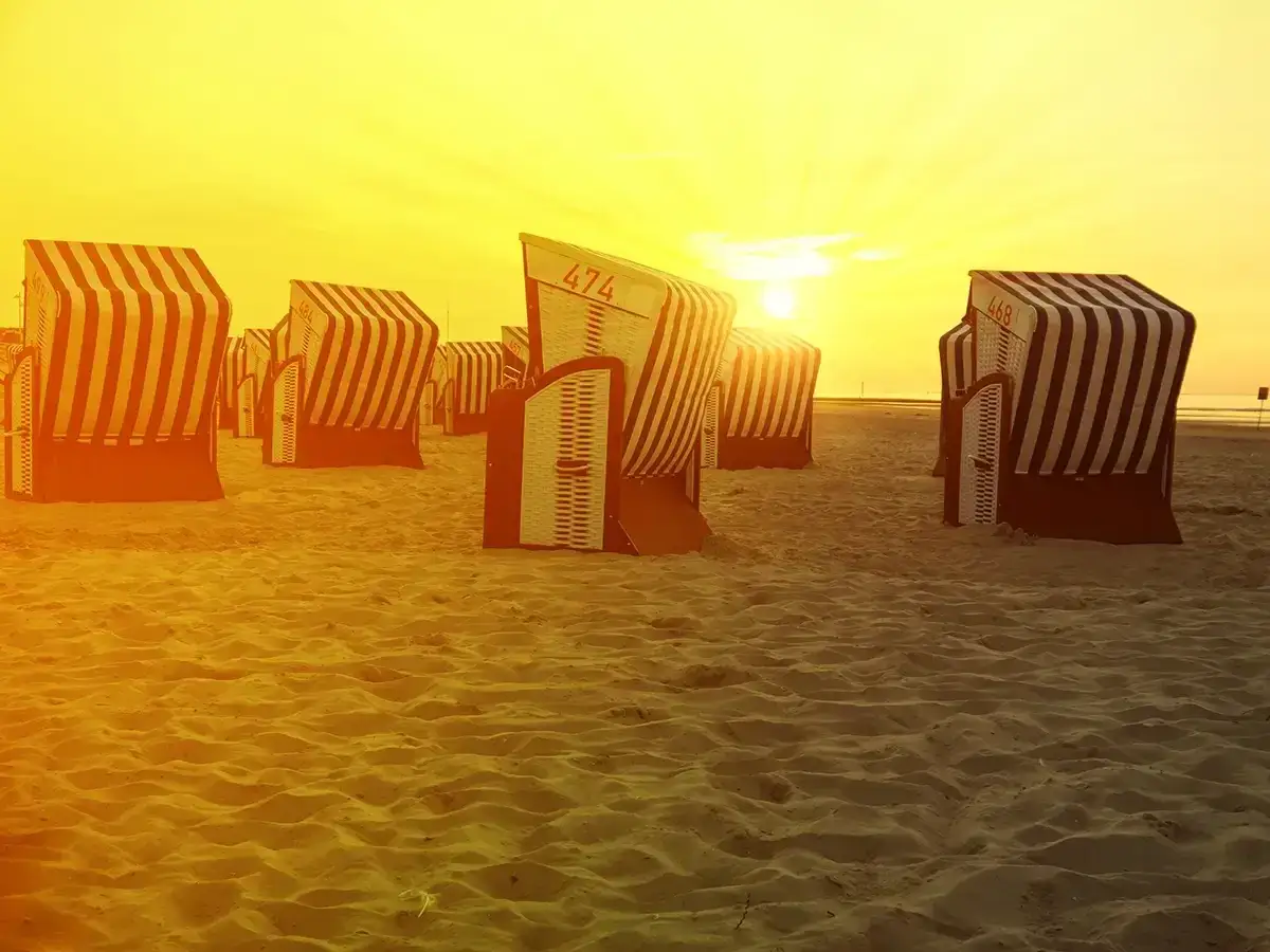 Zach&oacute;d słońca na piaszczystej plaży na wyspach fryzyjskich w Niemczech. Rzędy charakterystycznych koszy plażowych w pasy czekają na plażowicz&oacute;w.