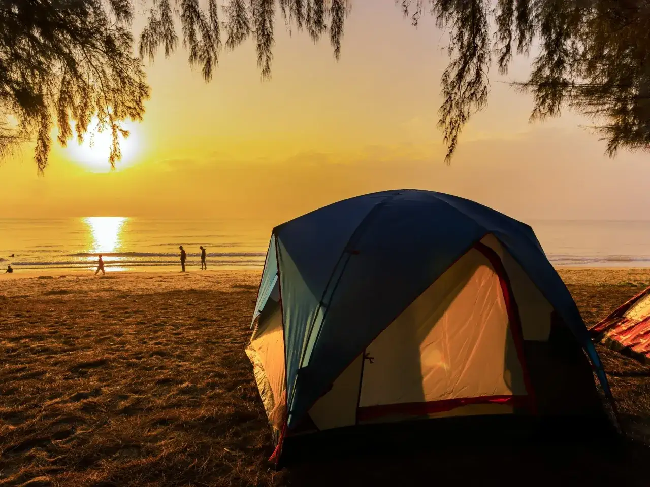 Namiot na plaży o zachodzie słońca. W tle widać morze i sylwetki ludzi. To idealne miejsce na pole kempingowe.