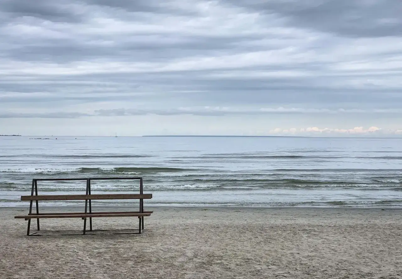 Pusta ławka na plaży, idealne ciche spokojne miejsce na weekend. Morze i zachmurzone niebo tworzą nastr&oacute;j.